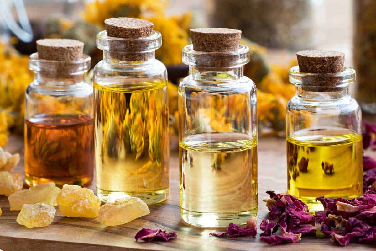 Bottles of essential oil with dried rose petals, chamomile, calendula and frankincense resin on a wooden table, Does Freezing Affect Essential Oils?