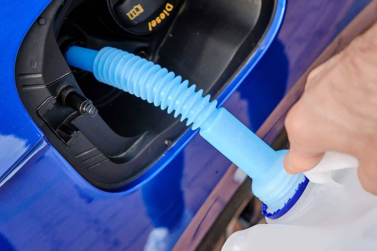 Close up filling of diesel exhaust fluid from canister into the tank of blue car