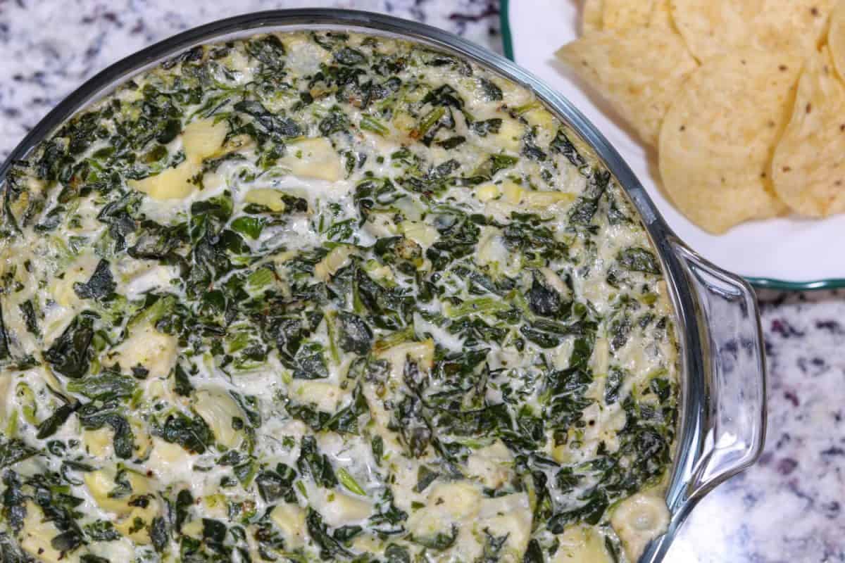 An up close photo of an artichoke dip with chips on the side