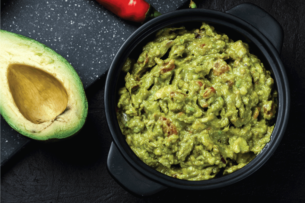 Bowl of guacamole with fresh ingredients on a black table