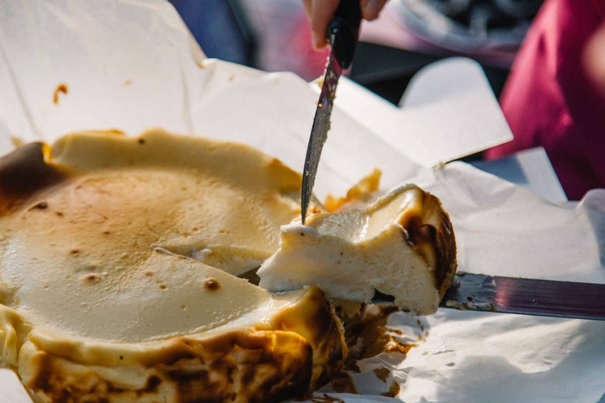 Mano femenina de cerca tomando una rebanada de pastel de queso quemado vasco tradicional casero de La Viña con espátula en la mesa