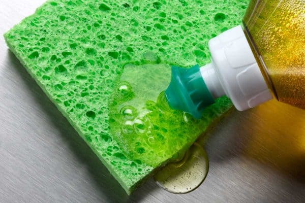 Dish soap being squeezed onto green sponge in aluminum sink, What Happens If Dish Soap Freezes?