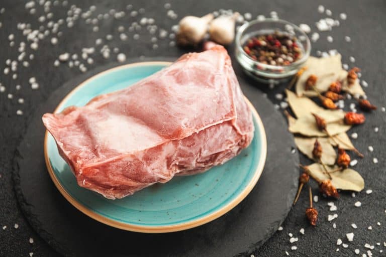 Frozen piece of raw meat on plate on black table,Does Freezing Pork Make It Tough?