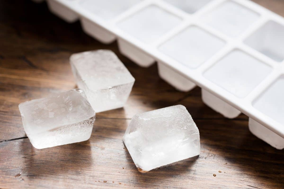 Ice cube tray filled with ice cubes and three lose ice cubes against dark wood