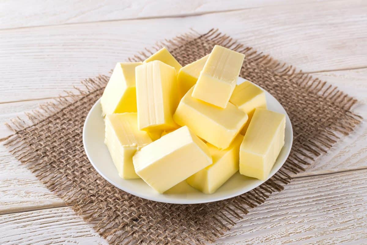 Rectangular pieces of fresh yellow butter on a white saucer over a white wooden table