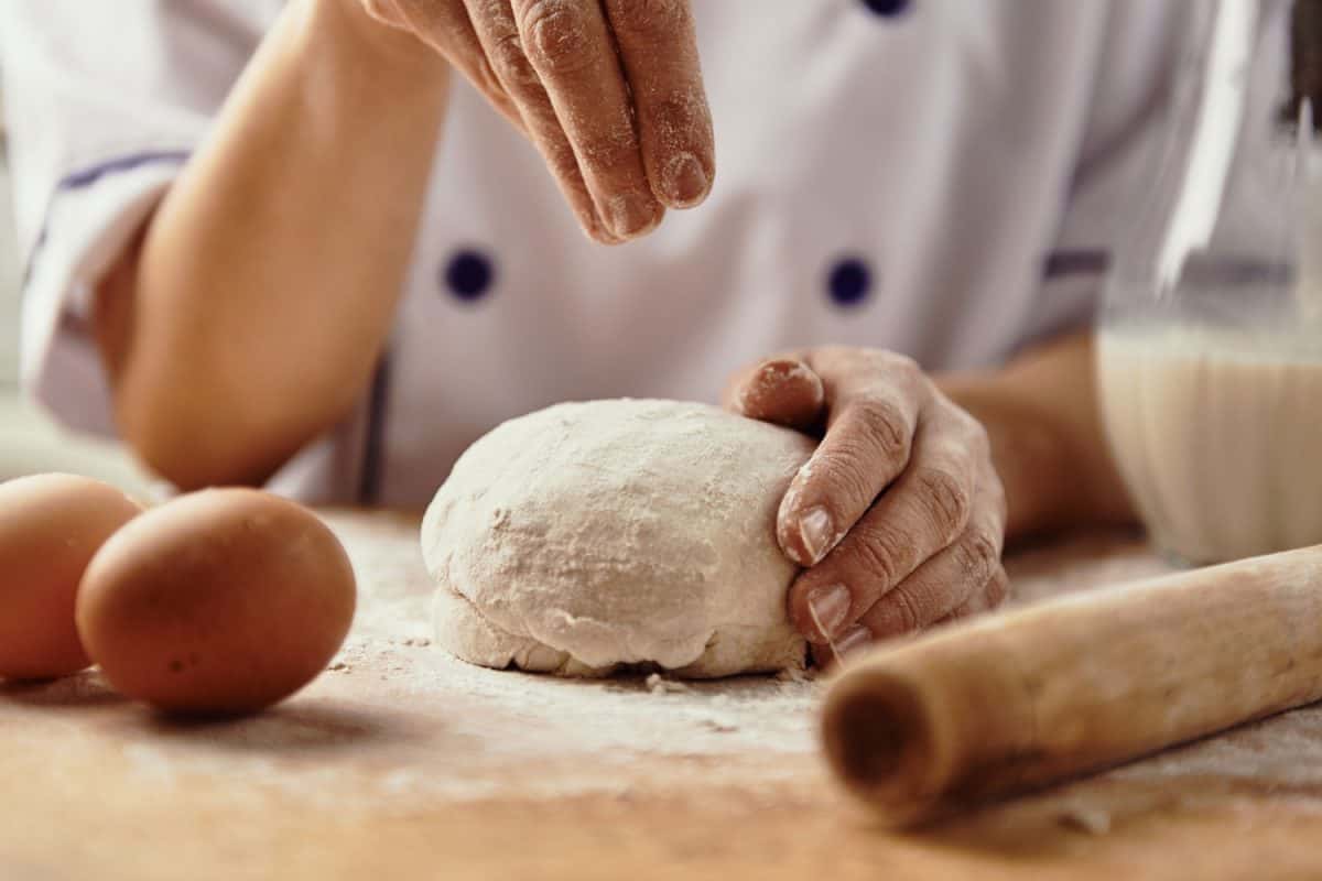 A Chef pouring flour on the dough to make it flowy