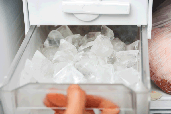 A woman opens an ice maker tray in the freezer to take ice cubes to cool drinks. How To Clean Your Freezer Ice Maker