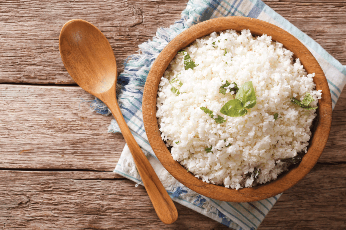 Cauliflower rice with basil in a wooden bowl, wooden spoon on the side