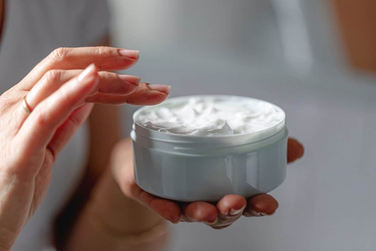 Close-up of woman using moisturizing cream for clean and soft skin, holding cream jar in hands