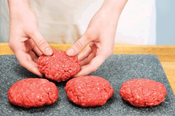 Cooking with ground beef, lady handling burger patties on a large dish. How Long To Defrost Burgers At Room Temp
