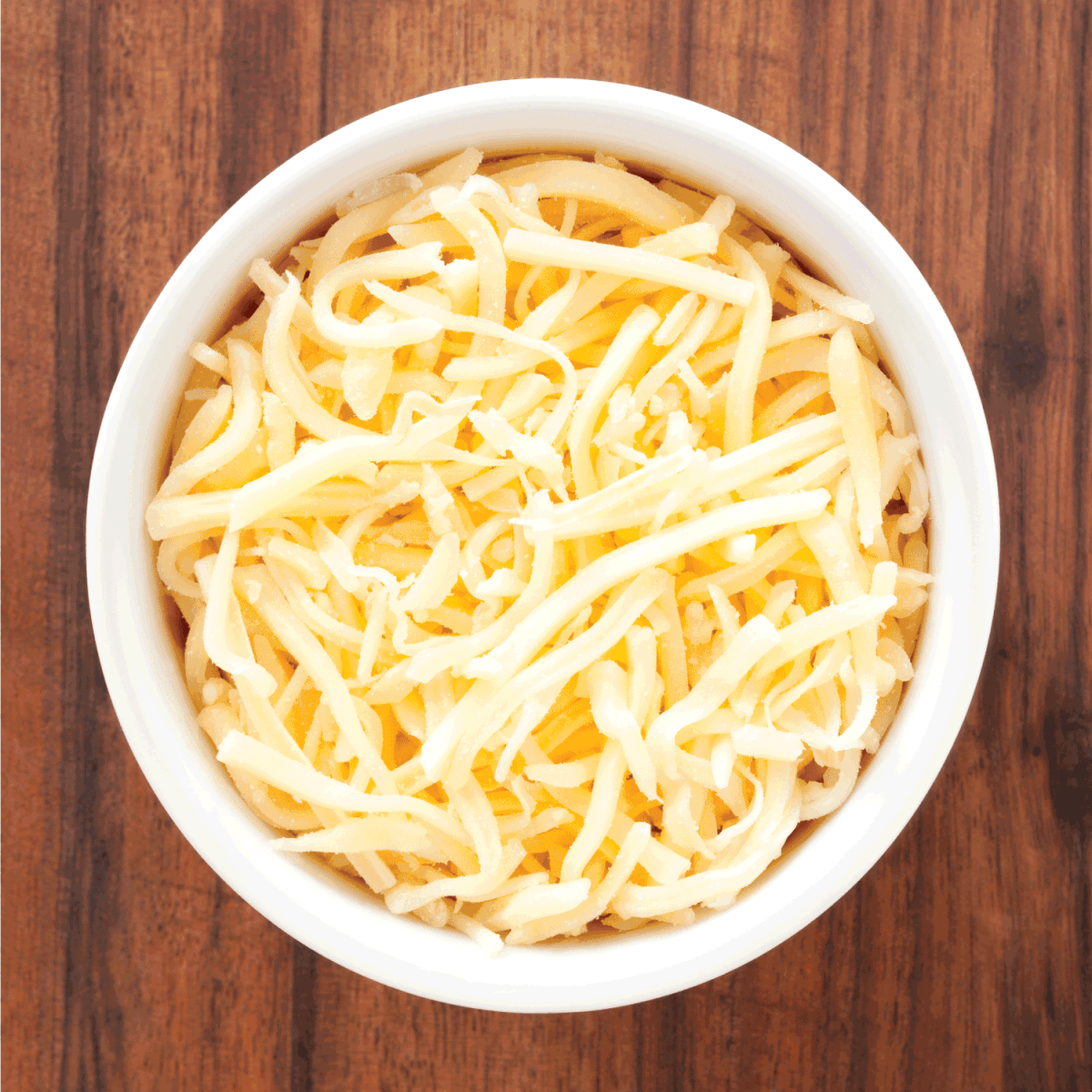 Top view of white bowl full of grated cheese