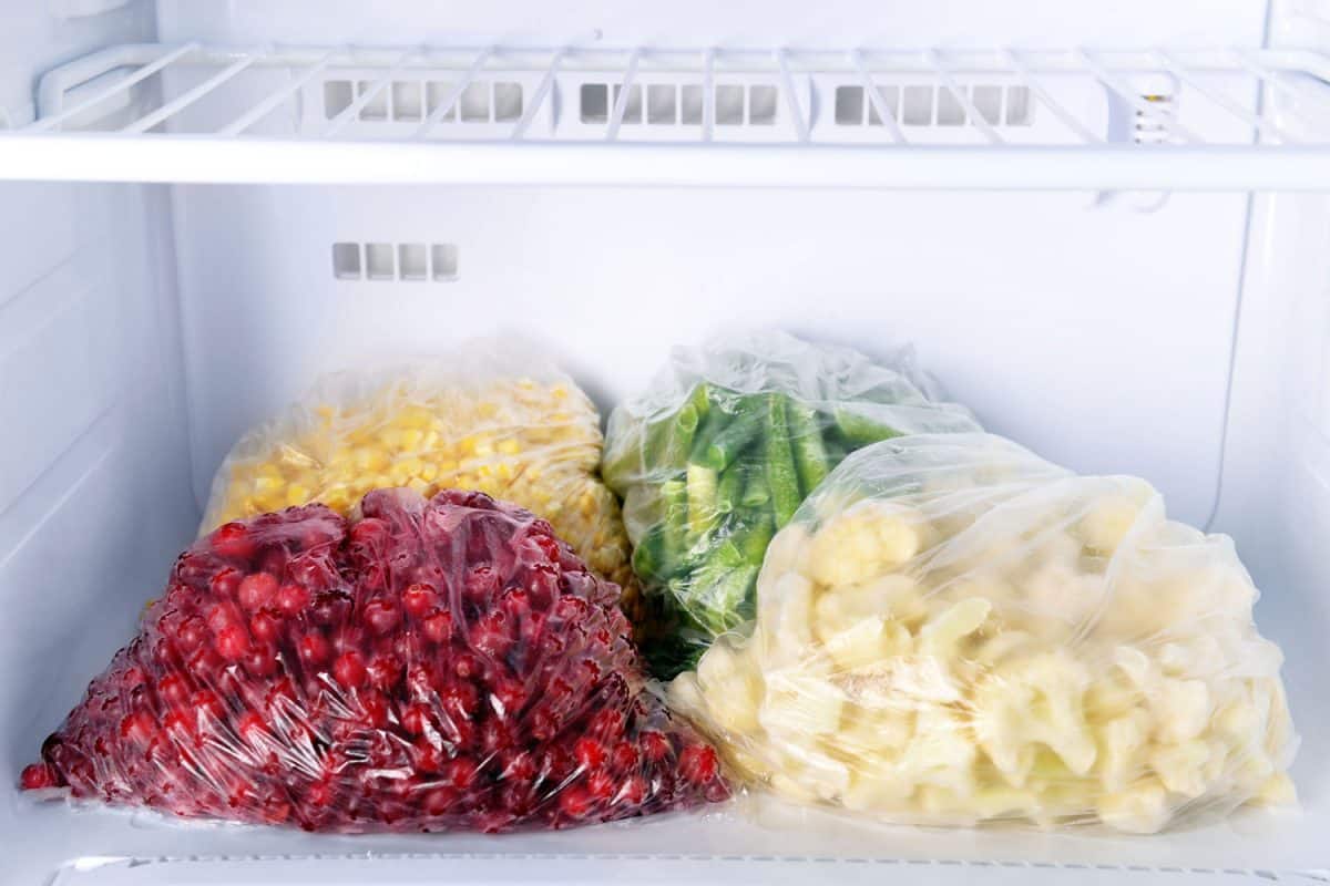 A small chest freezer with small berries, potatoes, and corn