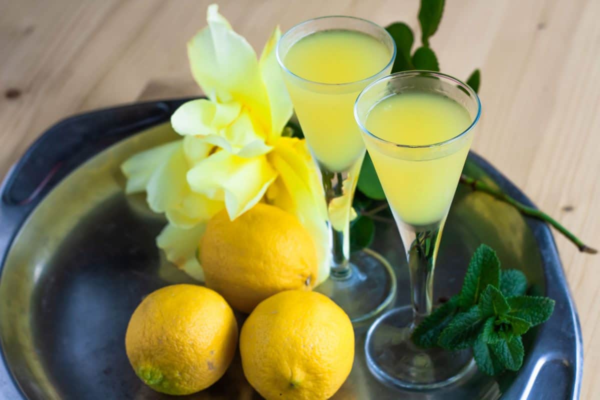 Two small wine glasses with lemoncello, mint leaves, and lemons on a small stainless steel plate