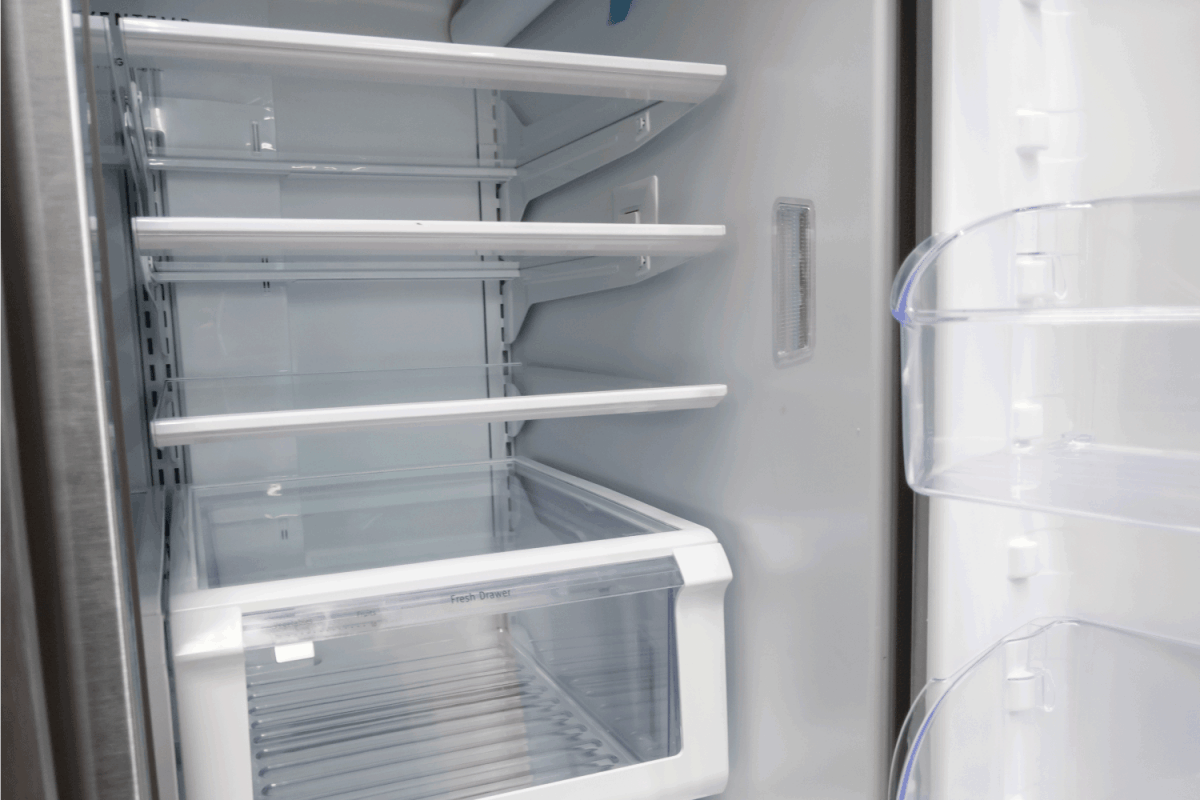 View of a white, empty fridge with the door wide open to see several shelves and drawers devoid of food