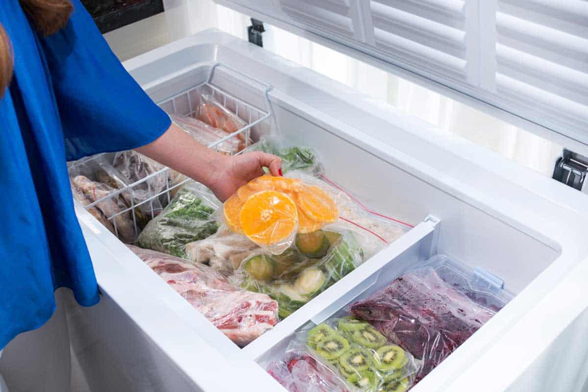 A woman putting food into a chest freezer, At What Temperature Should A Chest Freezer Be?