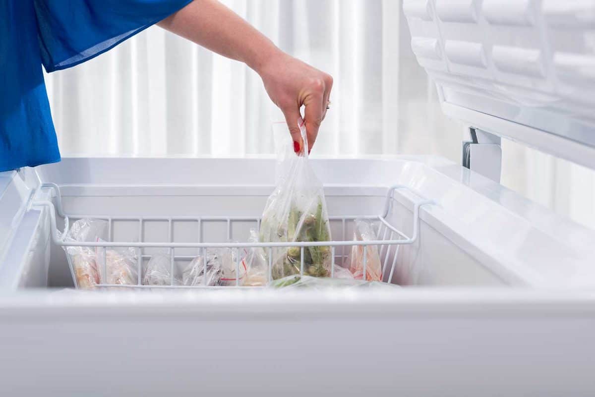 A woman putting some vegetables in a chest freezer