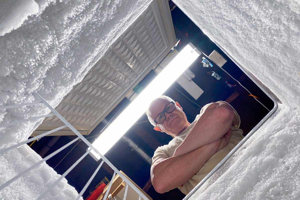 Frustrated man looking down at a defrosting chest freezer, How To Prevent Ice Buildup In Chest Freezer