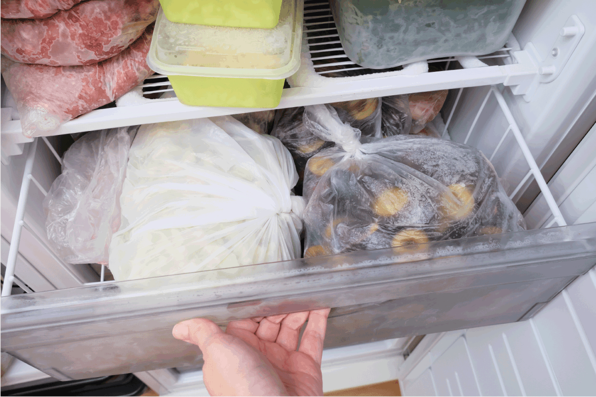 A hand opening a drawer of a freezer with frozen foods, long-term food storage and inventory at home.
