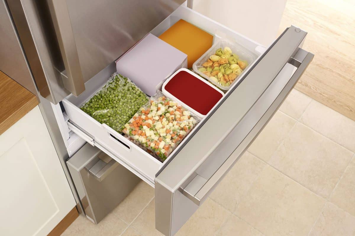 A small freezer drawer with green peas and other vegetables