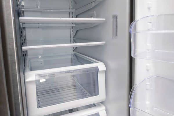 View of a white, empty fridge with the door wide open to see several shelves and drawers devoid of food, Can You Put Freezer Drawers In The Dishwasher?