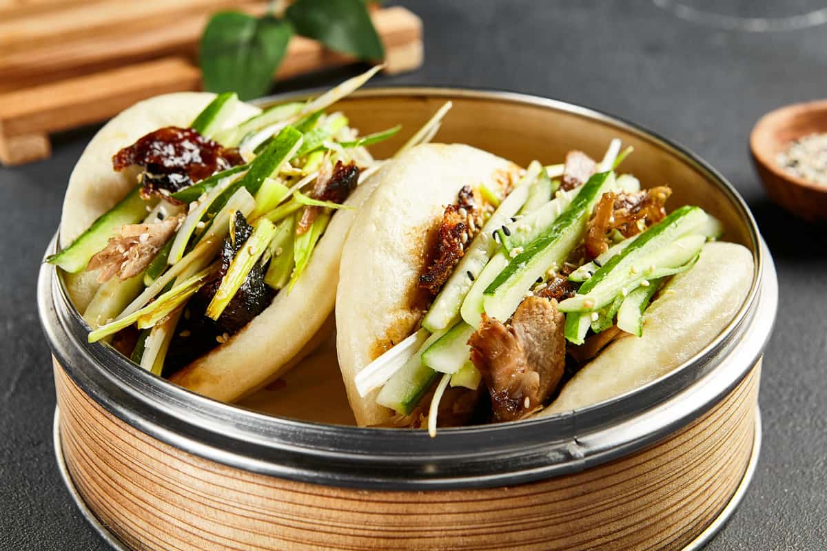 Bao buns with roasted chicken mixed with sliced cucumbers in a bamboo steamer