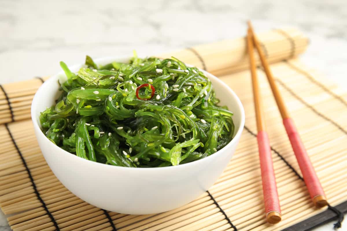 A bowl of seaweed salad drizzled with sesame seed and chopsticks on the side