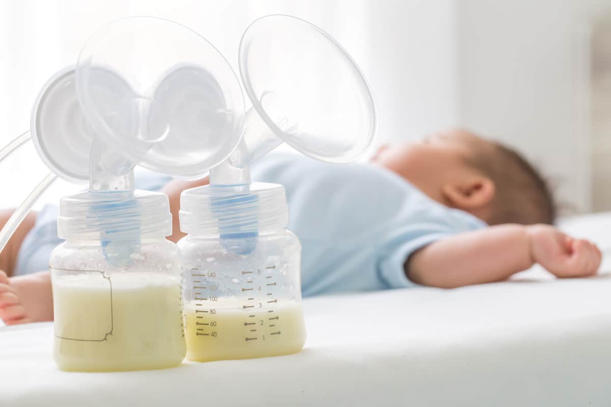 Breast milk pump and baby lying on the white bed.