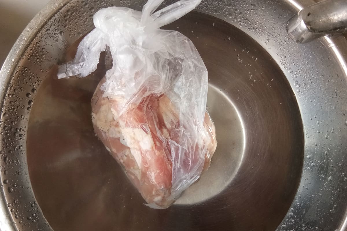 Defrosting chicken on a stainless bowl with water
